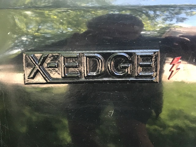 Close-up of XEDGES emblem and red lightning bolt emblem on a dark vehicle.