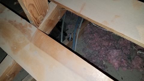 1985 Ford Bronco - This image shows the interior of an attic space with wooden beams and pink insulation. There are also some electrical wires and a metal bol…