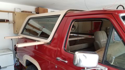 1985 Ford Bronco - A red Ford Bronco is parked in a garage with its removable top section being held in place by wooden beams. The interior shows a tan seat a…