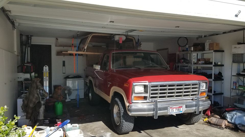Red 1980s pickup truck parked in a garage with another vehicle on top.