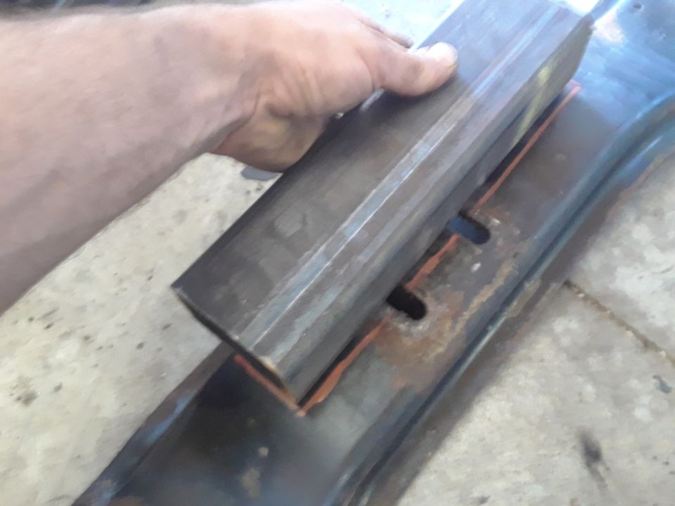 Hand holding a metal bar over a rusty metal part with an orange outline.