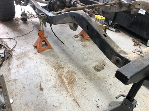 1992 Jeep Wrangler - The frame of a Jeep Wrangler is supported by orange jack stands on a concrete floor. Various mechanical parts and wiring are visible around…