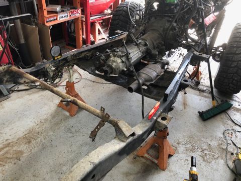 1992 Jeep Wrangler - The frame of a Jeep Wrangler is supported by orange jack stands in a garage. The transmission and exhaust system are visible, along with th…