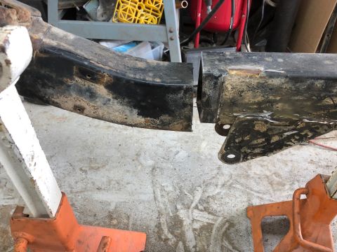 1992 Jeep Wrangler - A heavily rusted and dirty black metal frame part, likely from a vehicle's chassis, is supported by two orange jack stands. The frame appea…