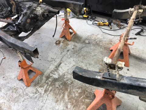 1992 Jeep Wrangler - A vehicle frame and drivetrain are supported by orange jack stands on a concrete floor. Tools, including an angle grinder and a drill, are…