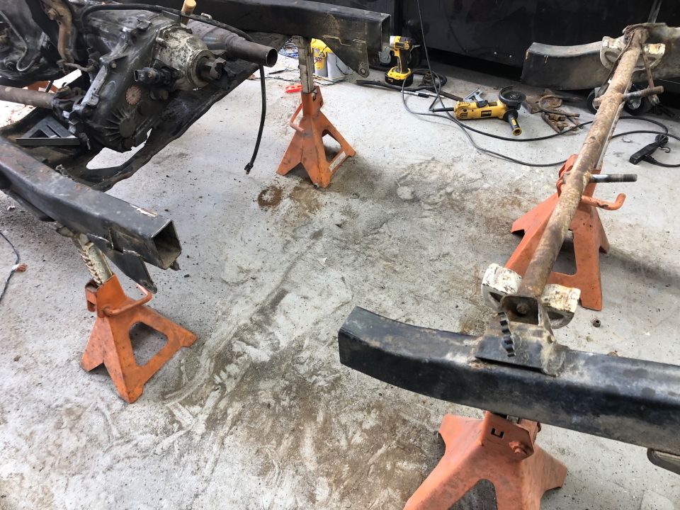 Vehicle frame and drivetrain on jack stands with tools in background.