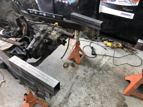 1992 Jeep Wrangler - A Jeep Wrangler's transmission and transfer case are supported by jack stands in a garage setting. Metal tubing, an angle grinder, and othe…