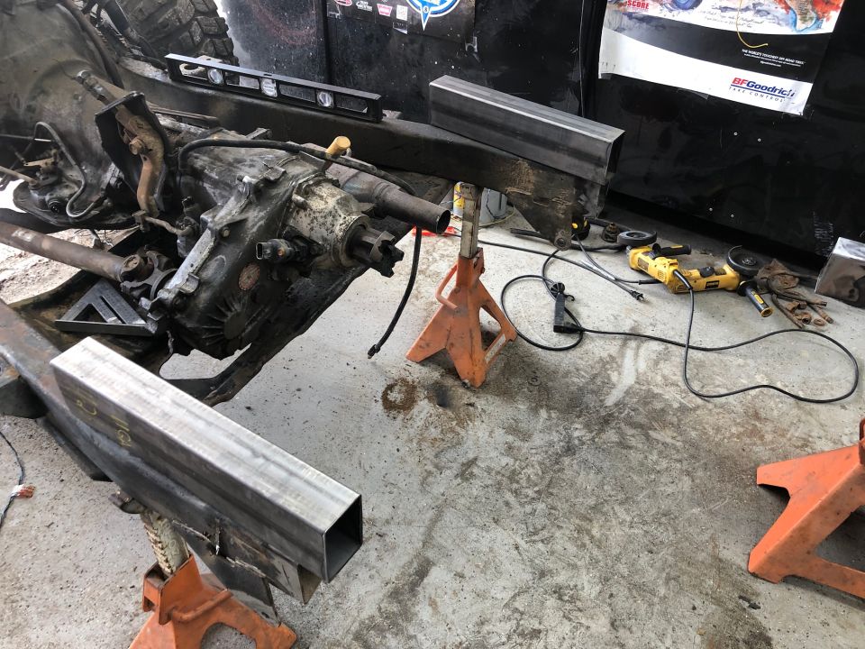 Jeep Wrangler transmission and transfer case on jack stands with tools nearby.