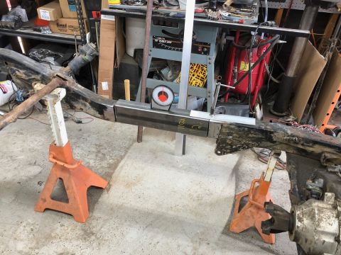 1992 Jeep Wrangler - A Jeep Wrangler frame is supported by jack stands in a workshop setting. Metal bracing is being welded to the frame, with a level and angle…