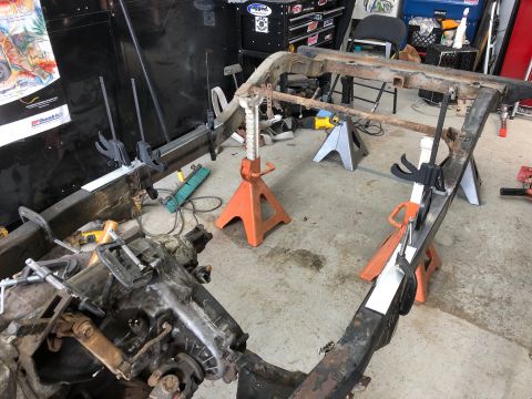 1992 Jeep Wrangler - A Jeep Wrangler frame is supported by jack stands in a garage setting. Metal plates are clamped to the frame, suggesting ongoing modificati…