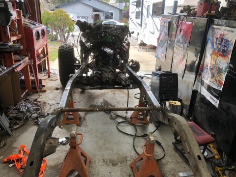 1992 Jeep Wrangler - A Jeep Wrangler frame is elevated on jack stands in a garage with an engine and transmission assembly mounted above it. A welding machine a…