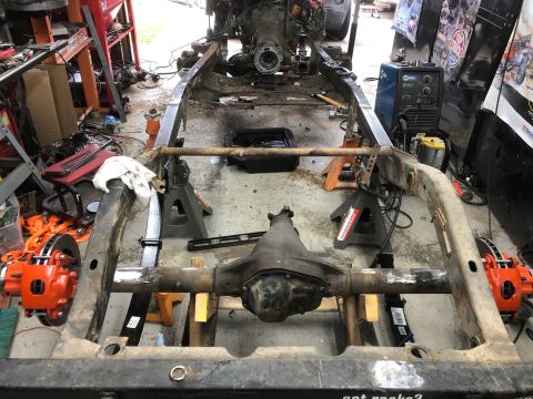 1992 Jeep Wrangler - A Jeep Wrangler frame is supported by jack stands in a garage setting. The rear axle with bright orange brake calipers is visible, along wi…