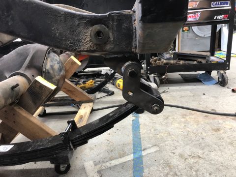 1992 Jeep Wrangler - A close-up view of a vehicle's rear axle and leaf spring suspension system, supported by wooden blocks and casters. The frame and suspensio…