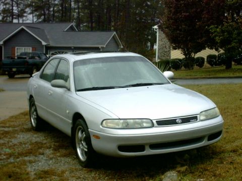 1995 Mazda 626 - A silver 1995 Mazda 626 sedan is parked outside a house, with another vehicle visible in the driveway.