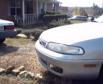 1995 Mazda 626 - A silver sedan is parked in a driveway with another car and a limousine in the background.