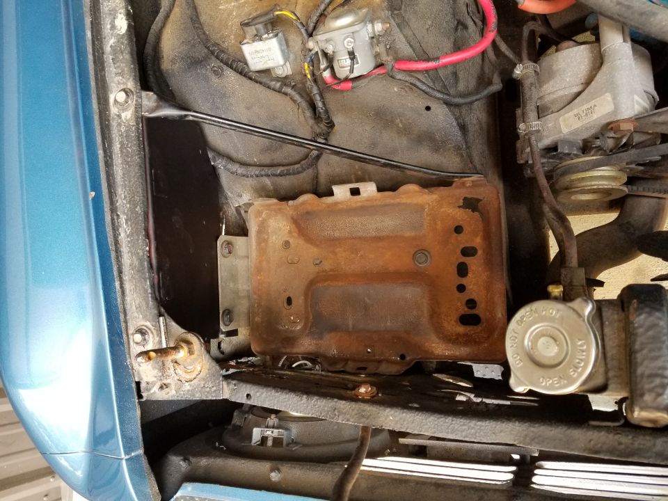 Rusty battery tray and engine bay components on a blue vehicle