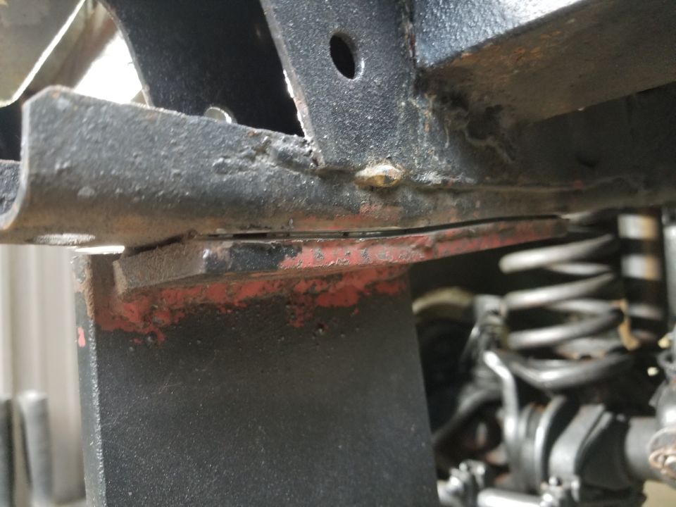 Close-up of welded steel frame bracket with red primer and surface rust near coil spring