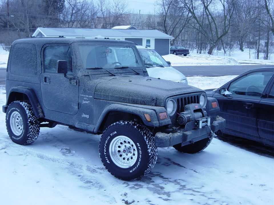 Dirty black Jeep Wrangler with winch and BFGoodrich tires parked in snow