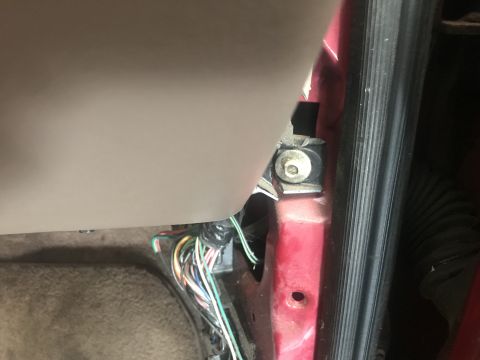 1994 Ford Bronco - A close-up view of the interior door jamb area of a red vehicle, showing wiring harnesses and a metal bracket secured by a bolt.