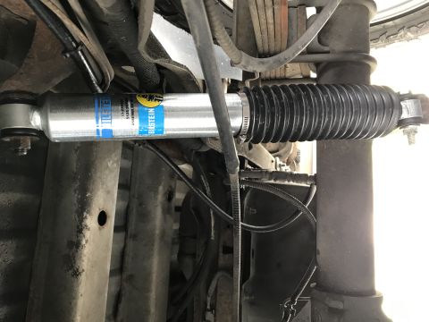 1995 Ford Bronco - A close-up, low-angle shot of a new silver Bilstein shock absorber with a black rubber boot installed on the underside of a vehicle. The sh…