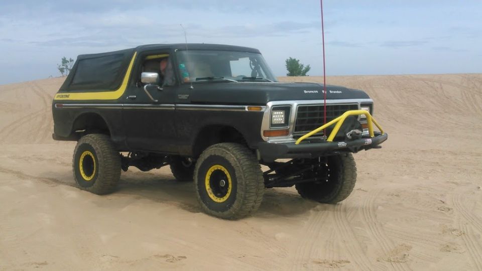 Lifted black 1978 Ford Bronco with yellow accents on sand dunes.