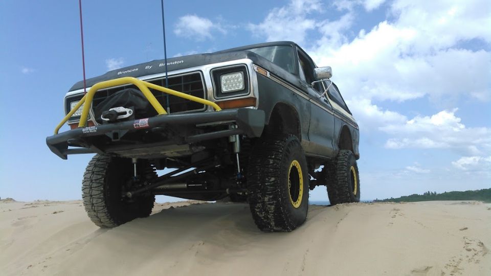 Lifted 1978 Ford Bronco with yellow brush guard and off-road tires on a sand dune.