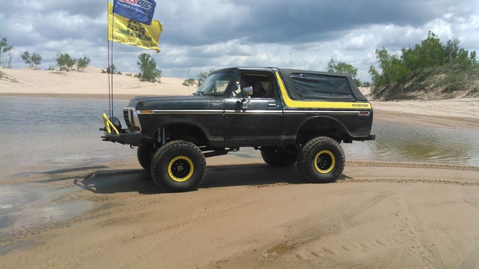 1978 Ford Bronco with yellow accents and flags on a sandy beach.