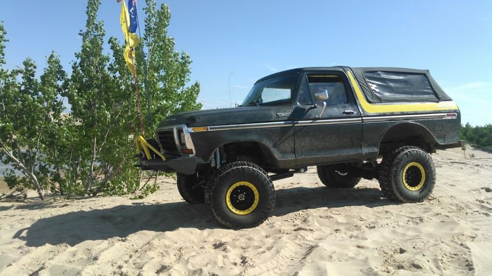 Lifted dark green 1978 Ford Bronco with yellow accents and soft top on a sandy dune.