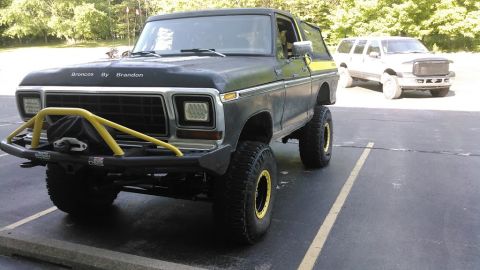 1978 Ford Bronco - A lifted, black 1978 Ford Bronco with a yellow roll cage and a custom front bumper is parked in a lot next to a white SUV. The Bronco has l…