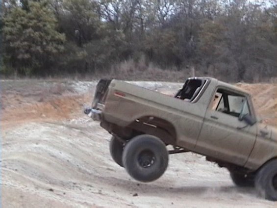Tan lifted truck with roll bar nose-down on a steep dirt bank, front wheel lifted