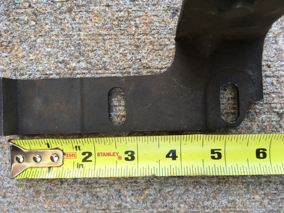 Metal vehicle part with two oval cutouts over a yellow measuring tape.