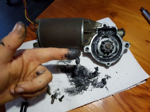 1978 Ford Bronco - A person's hand covered in black grease is shown next to a disassembled starter motor with its gear exposed and heavily greased. The starte…