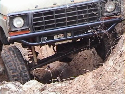 1978 Ford Bronco - 1978 Ford Bronco's front end is visible, stuck in a ditch with off-road modifications.