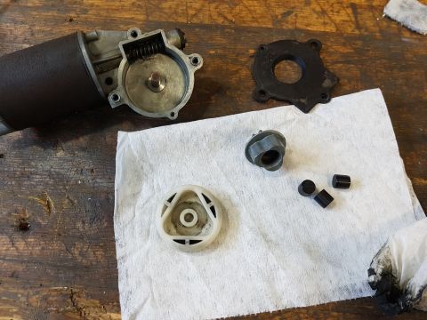 1978 Ford Bronco - Disassembled windshield wiper motor components are laid out on a white paper towel on a wooden workbench. The main motor housing is visible…