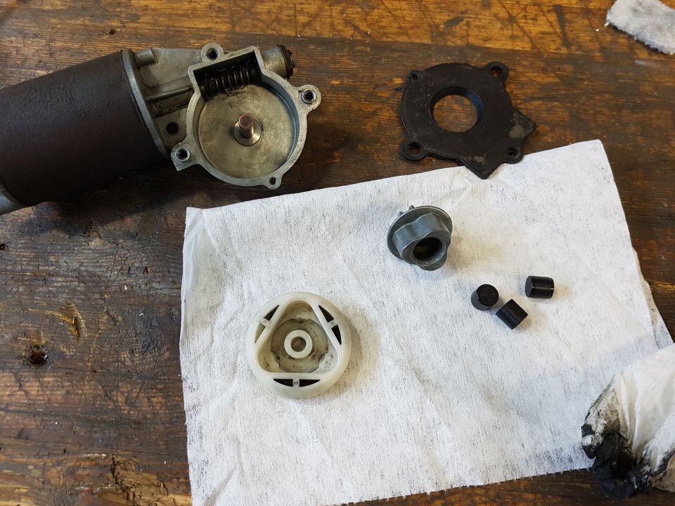 Disassembled windshield wiper motor parts on a workbench.