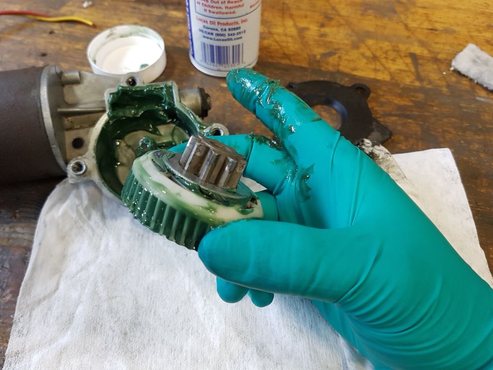 Gloved hand holding greased gear next to motor housing and open grease container