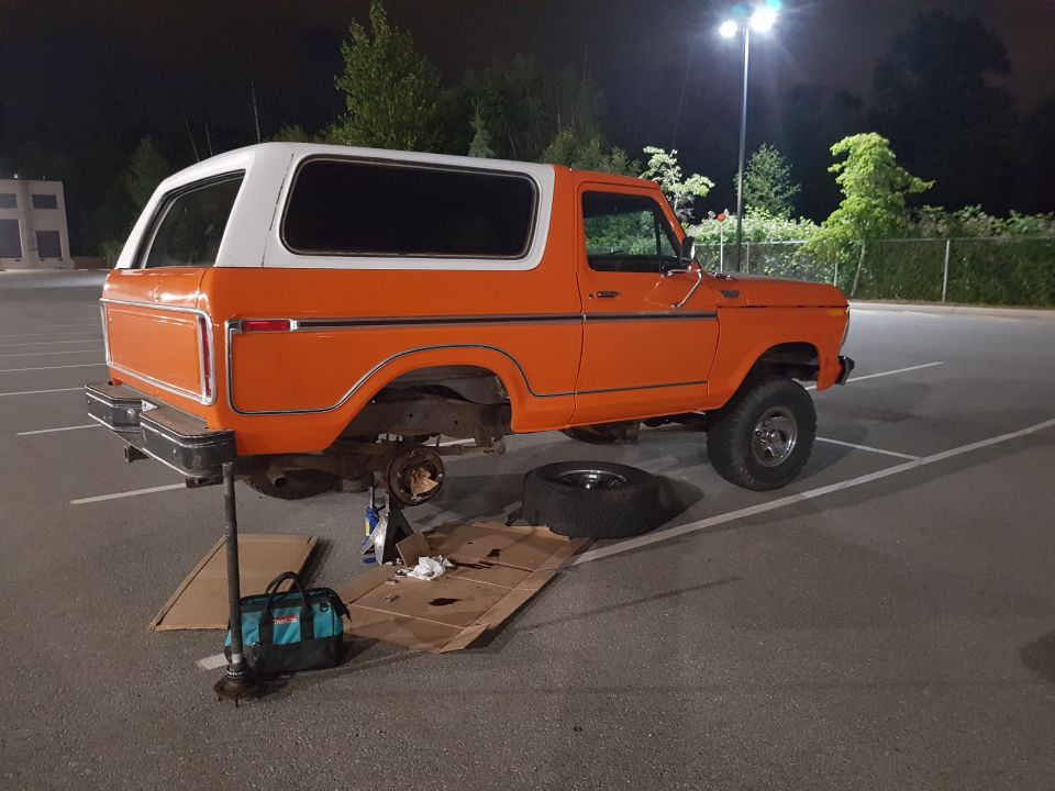 Orange Ford Bronco on jack stands, rear wheel off, parked in lot at night
