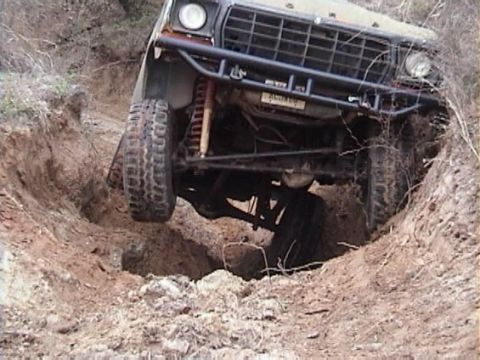 1978 Ford Bronco - A 1978 Ford Bronco navigates a challenging off-road terrain, its front tires deep in a ditch.
