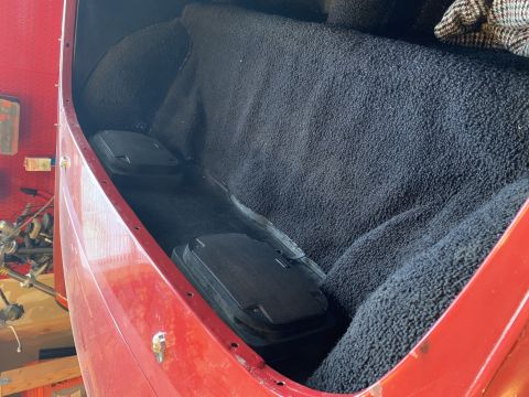 1979 Ford Bronco - The interior of a red vehicle shows black carpeting and two storage compartments in the cargo area.