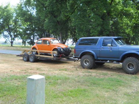 1992 Ford Bronco - A blue 1992 Ford Bronco tows a trailer carrying an orange Volkswagen Beetle on a sunny day.
