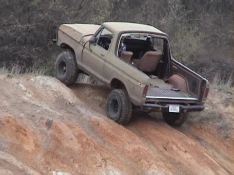 1978 Ford Bronco - Tan/olive lifted full-size Ford 4x4 with its removable hardtop off, flexing at an angle while climbing a steep red-clay dirt embankment. Br…