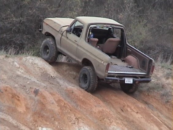 Tan topless lifted Ford 4x4 climbing a steep red clay dirt bank off-road