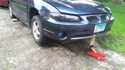 Blue Pontiac Grand Prix on a jack with wood blocks under the frame