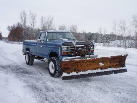 1994 Ford Bronco - A blue pickup truck equipped with a snow plow sits on a snow-covered road, ready for winter conditions.