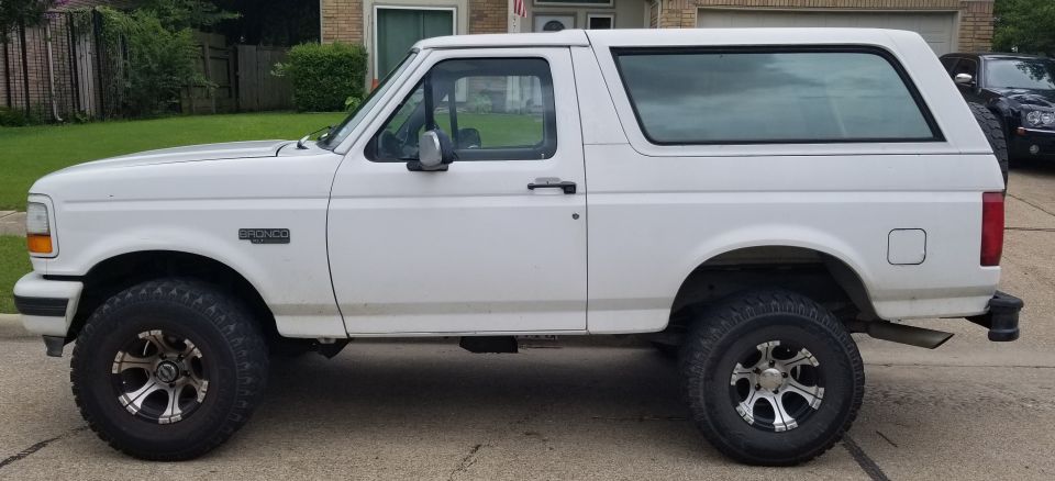 White Ford Bronco parked on a street, side view. Has aftermarket wheels and tires