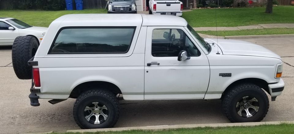 White Ford Bronco, side view, spare tire mounted on rear door, aftermarket wheels