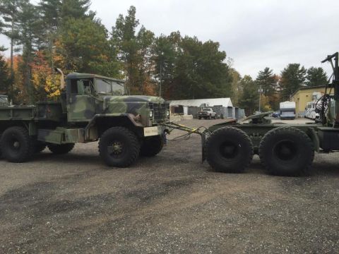 1992 Ford Bronco - A military truck with camouflage paint tows a trailer, seen from the side.