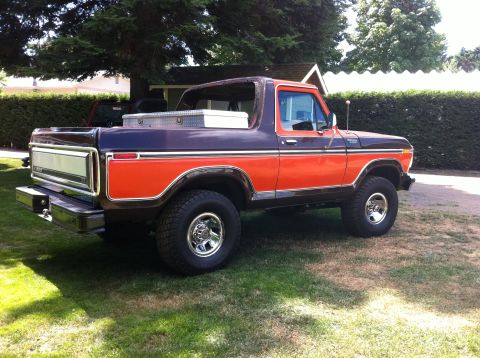 1978 Ford Bronco - This two-tone Ford Bronco is parked in a grassy yard with a hedge and house in the background.