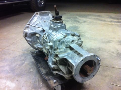 1978 Ford Bronco - A manual transmission is shown resting on a stand in a garage or workshop.