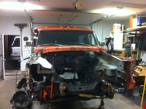1978 Ford Bronco - Orange truck chassis is disassembled in a garage, with another white vehicle visible in the background.